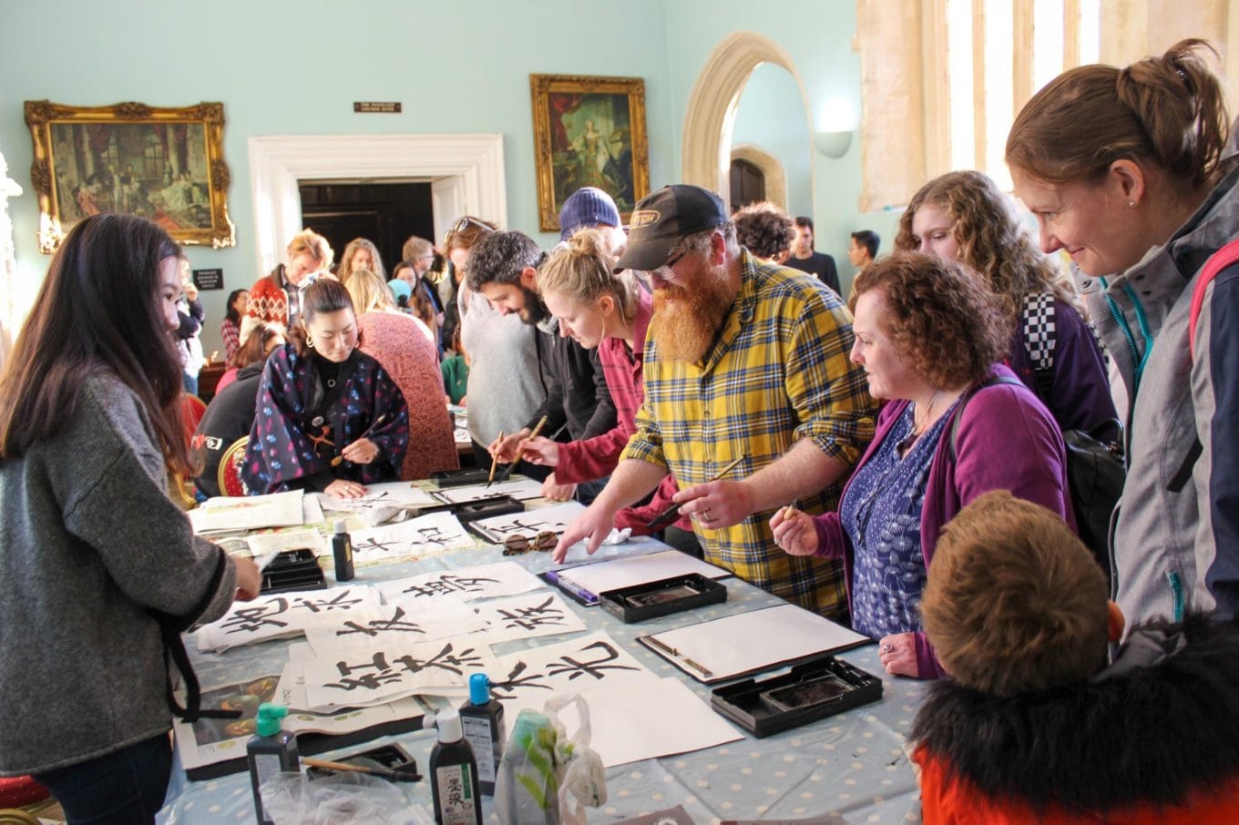 A crowd gathers around a table to practice calligraphy during the Bristol Japan Showcase