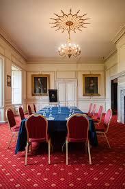 A grand mansion room with a chandelier and table and chairs set up for a meeting with water glasses on the table