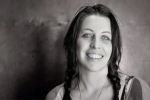 Headshot of a white woman with dark hair in plaits smiling at the camera