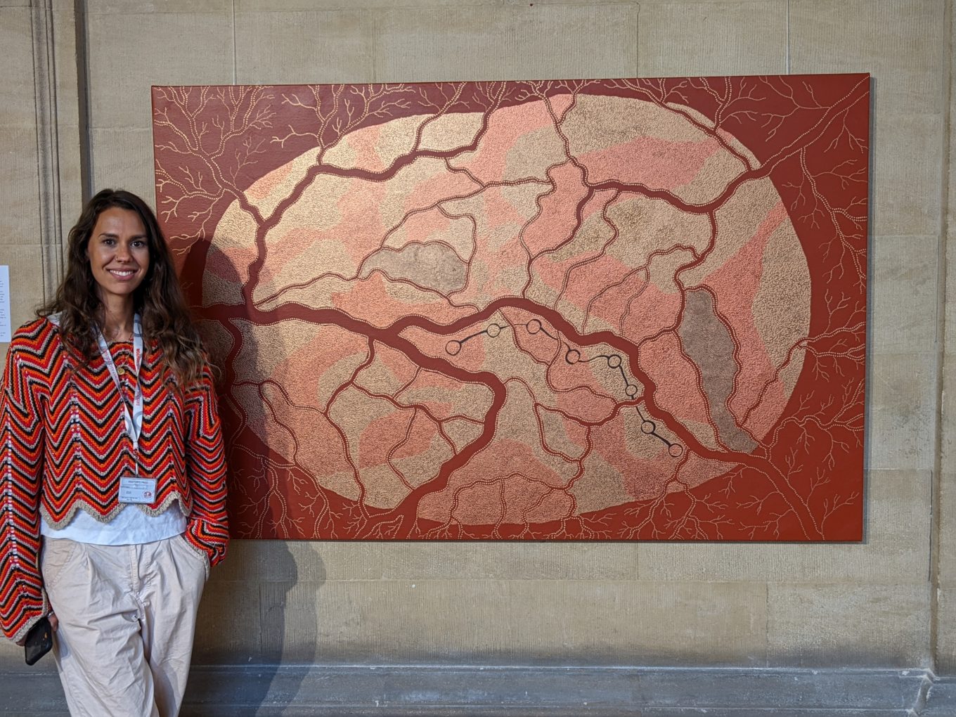 Artist Jasmine Coe standing in front of a large Native Australian artwork