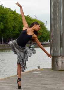 A ballet dancer pirouetting in a city location beside a river