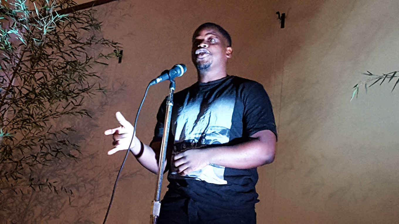 Sail Katebe, a Zambian born writer and performer, uplit, on stage performing poetry