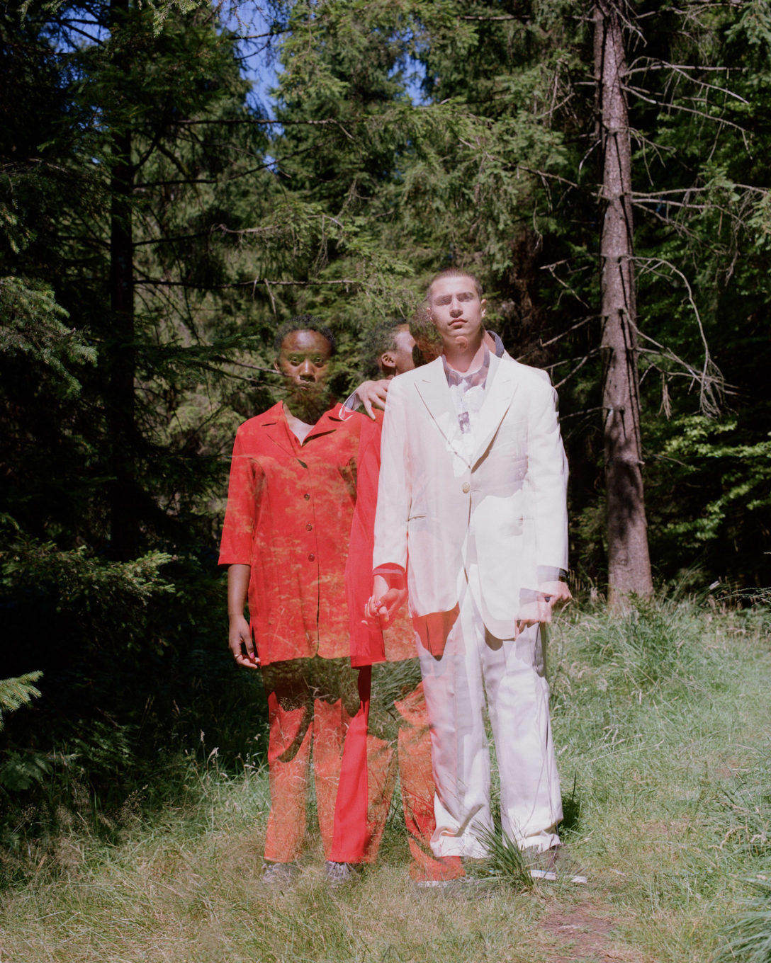 In the woods, a woman in red stands next to a man wearing white.