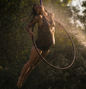 A woman hangs from a hoop surrounded by trees in the rain