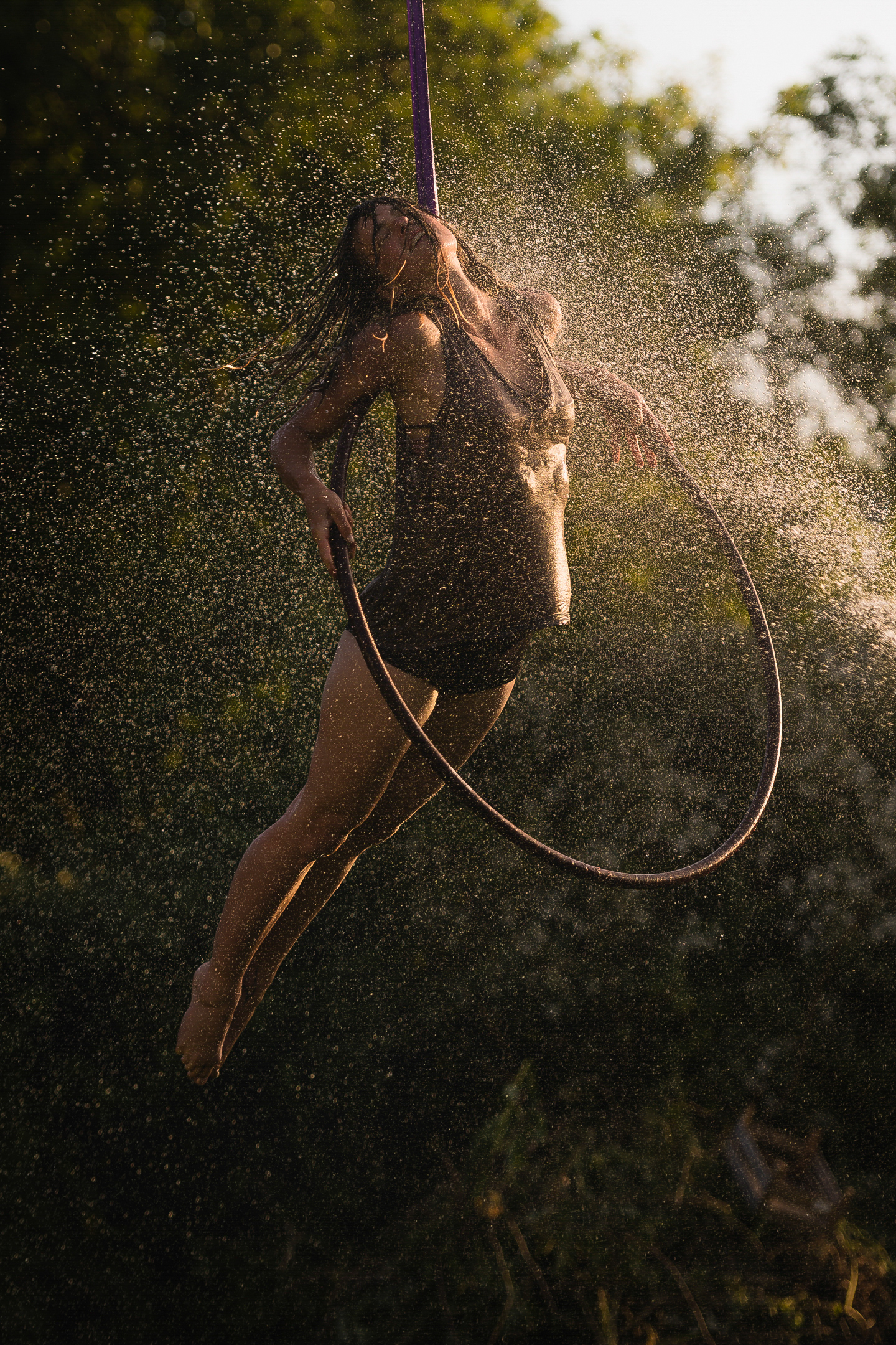 A woman hangs from a hoop surrounded by trees in the rain