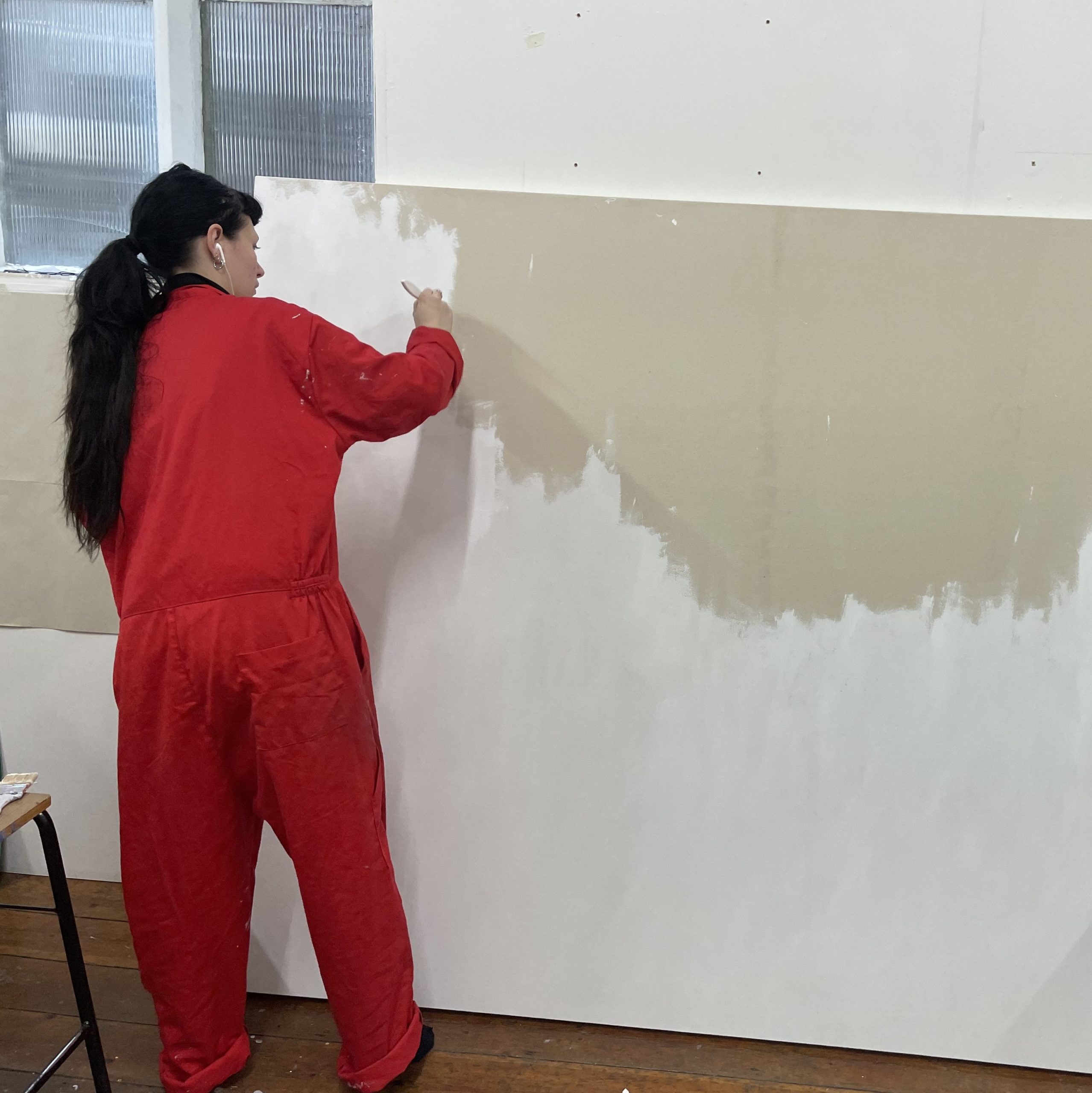 An artist in an orange jumpsuit paints a large board white
