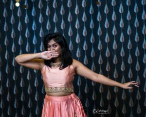 A bollywood dancer strikes a pose covering her mouth behind a patterned background