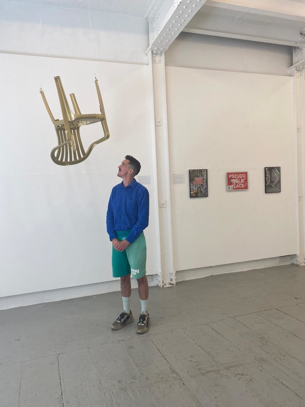 artist alaric hobbs standing beneath a gold plastic chair suspended from the ceiling