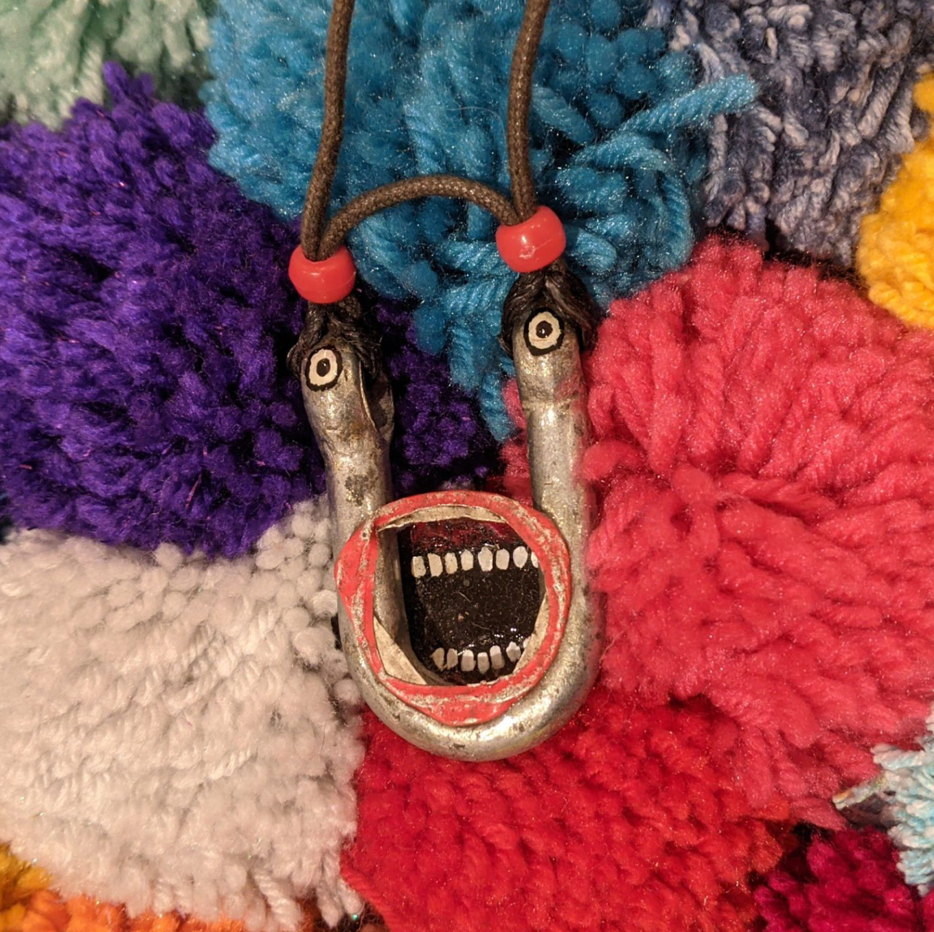 A small pendent featuring a screaming mouth sits on a bed of pom poms