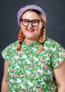 Profile photo of a woman in pigtails wearing glasses, a purple beret and a very jazzy top