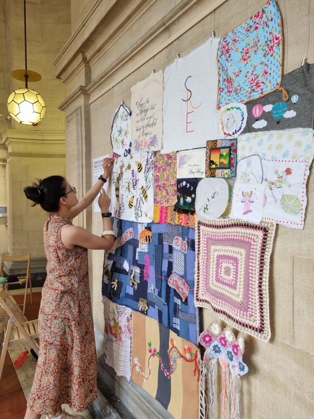 A woman pins embroidery work to a wall display