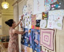 A woman pins embroidery work to a wall display