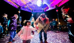 A woman and child dance under a glitter ball in a park podium