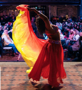 Text based poster with photo of a belly dancer on stage in front of an audience