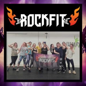 A group of women in exercise clothes pose holding a banner for a rockfit class