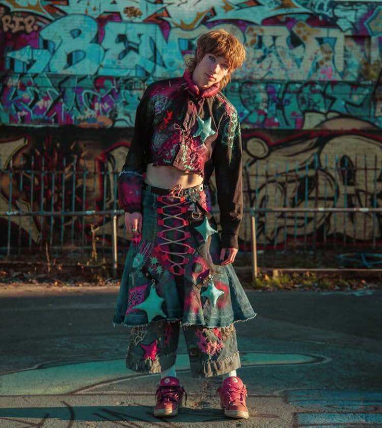 a whiter person stands in front of some graffiti wearing heavily embroidered, customised denim clothes