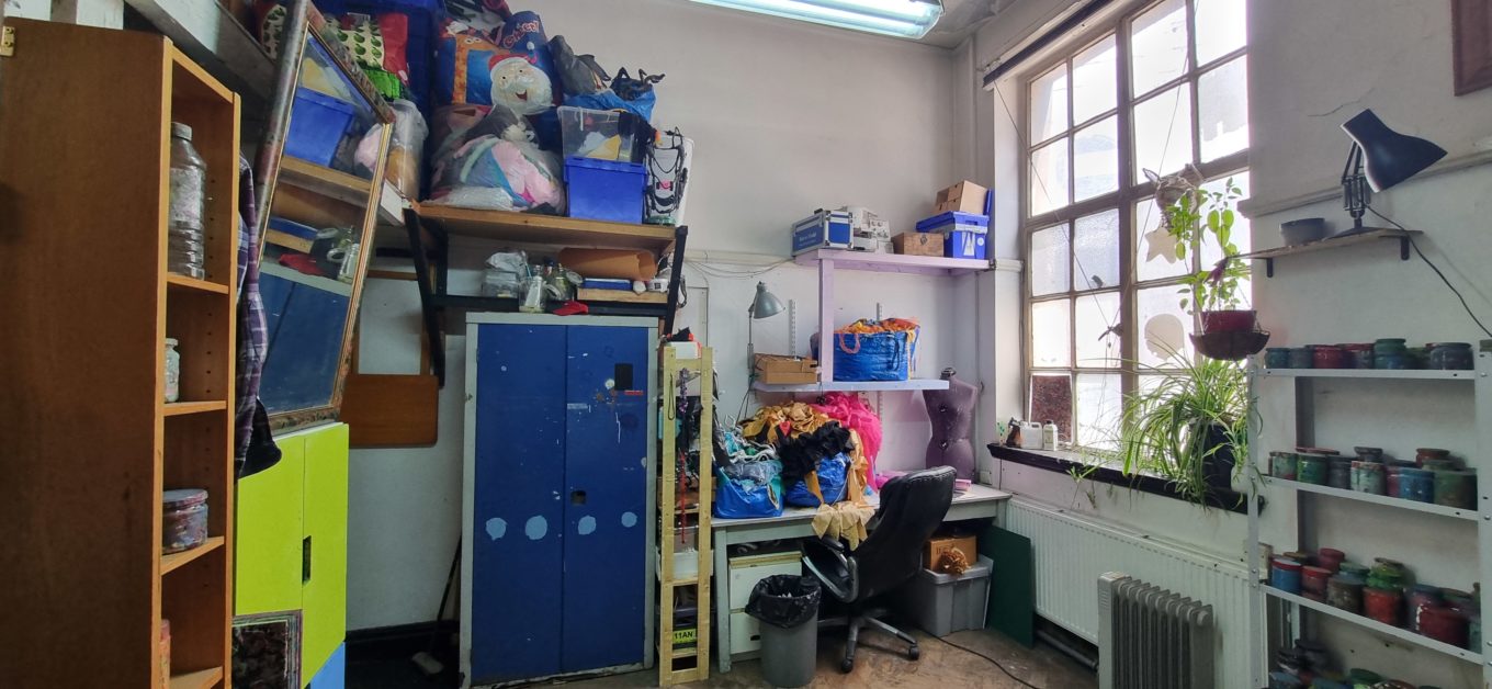 Photograph showing a desk and chair in a busy artists studio .