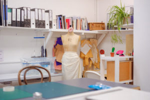 a sewing studio with files on shelves and a dress dummy