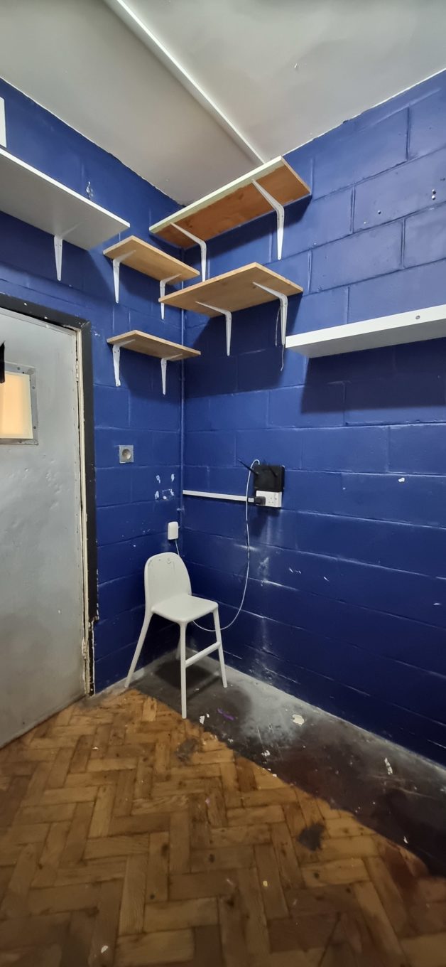 An empty blue-walled room with shelves and a chair in the corner