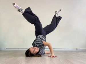 A woman strikes a break dance style move with her shoulder resting on the floor and her legs raised
