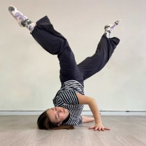 A woman strikes a break dance style move with her shoulder resting on the floor and her legs raised