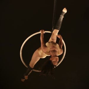 A woman does the splits while hanging in the middle of an aerial hoop