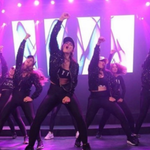 A group of dancers wearing caps, hoodies and leggings raise their fists in the air
