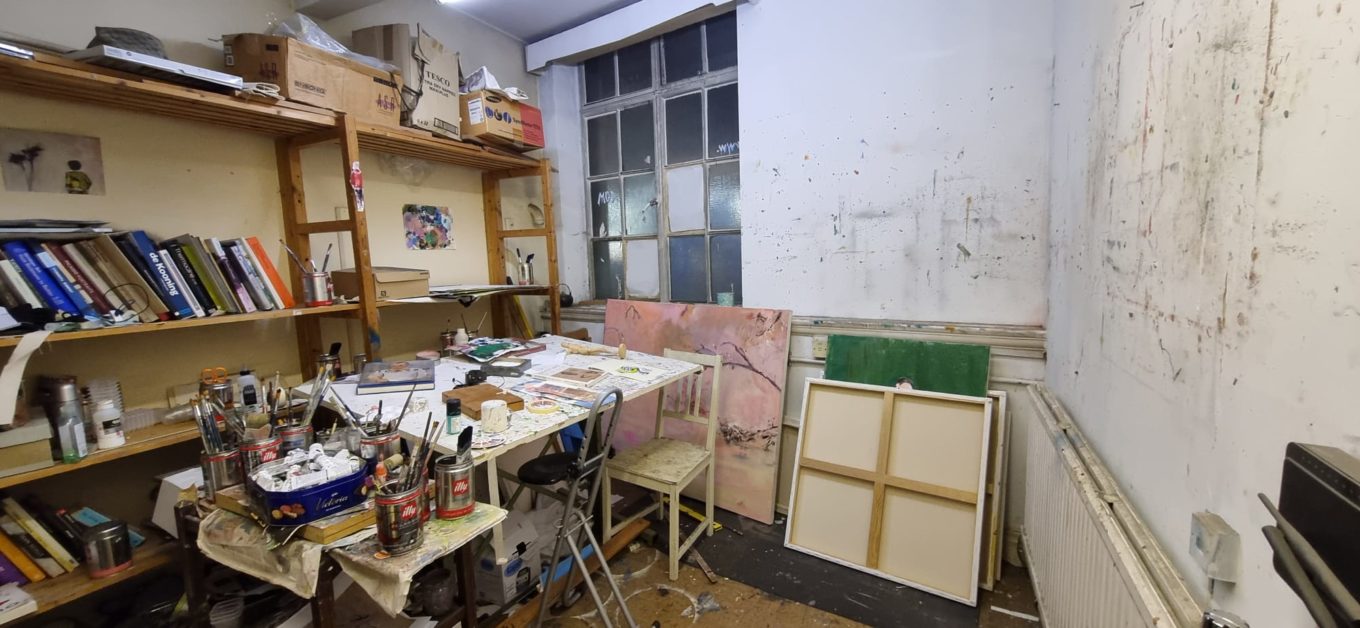 A busy artist studio with lots of paint paraphernalia on a table and shelves