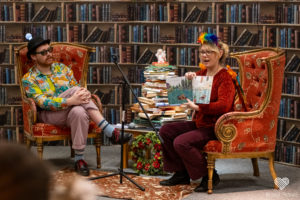 two people sit on large armchairs surrounded by books