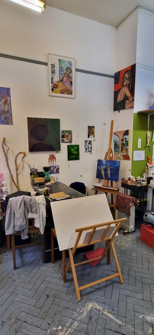 Photo of a corner of an artirts studio with paintings on the wall and mismatched furniture
