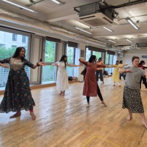 Photo of women dancing in a studio, most are wwearing traditional Indian dresses