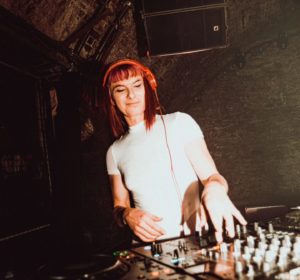 A woman with red hair is wearing headphones while DJing