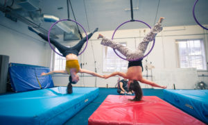 Two women hang upside down in aerial hoops