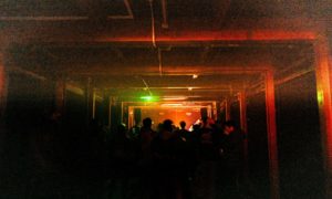 A dark night club with a crowd of people silhouetted by low lighting