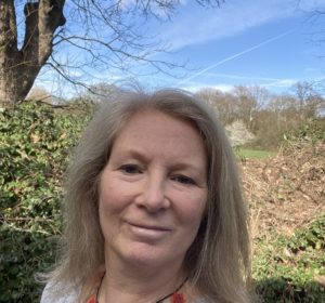 Photo selfie of a white woman standing in front of a garden with a blue sky