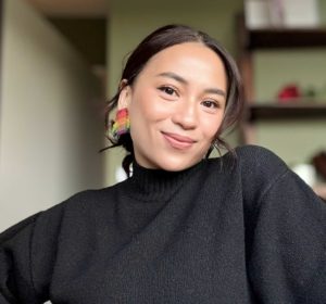 Headshot of a woman wearing a black turtleneck jumper and rainbow earrings